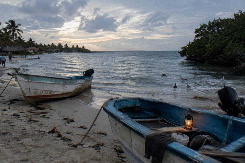 Small fishing boats resting on sand beside a calm Caribbean bay at dusk