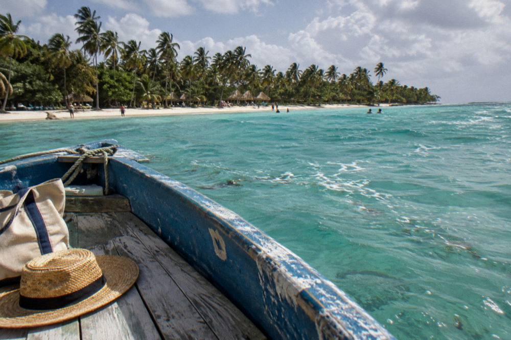 Beach bag and hat resting on the bow of a wooden boat in shallow turquoise water