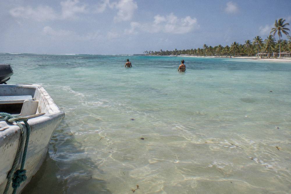 Shallow natural pool sandbar with calm clear water and distant palm island