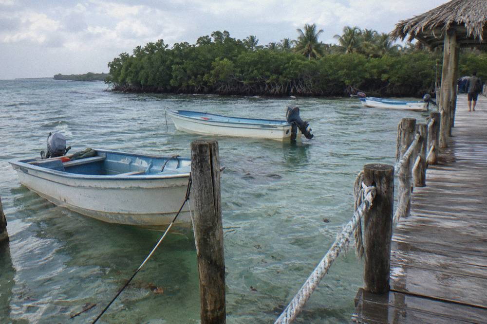 Small boats moored in clear shallow water beside a wooden dock