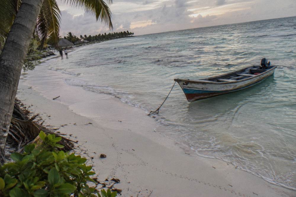 Empty white sand beach with a single wooden boat resting in shallow clear water