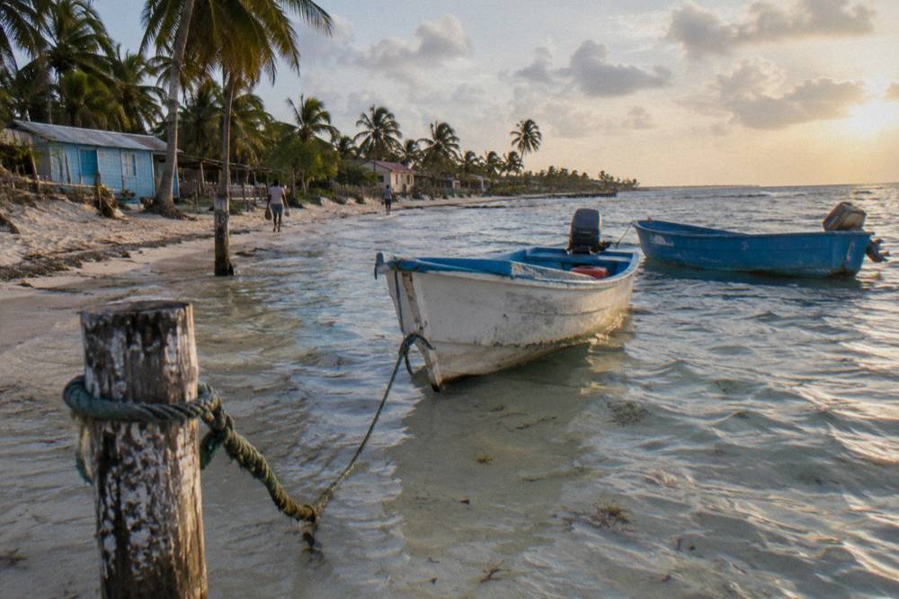 A calm Caribbean beach with clear shallow water and moored boats in late afternoon light
