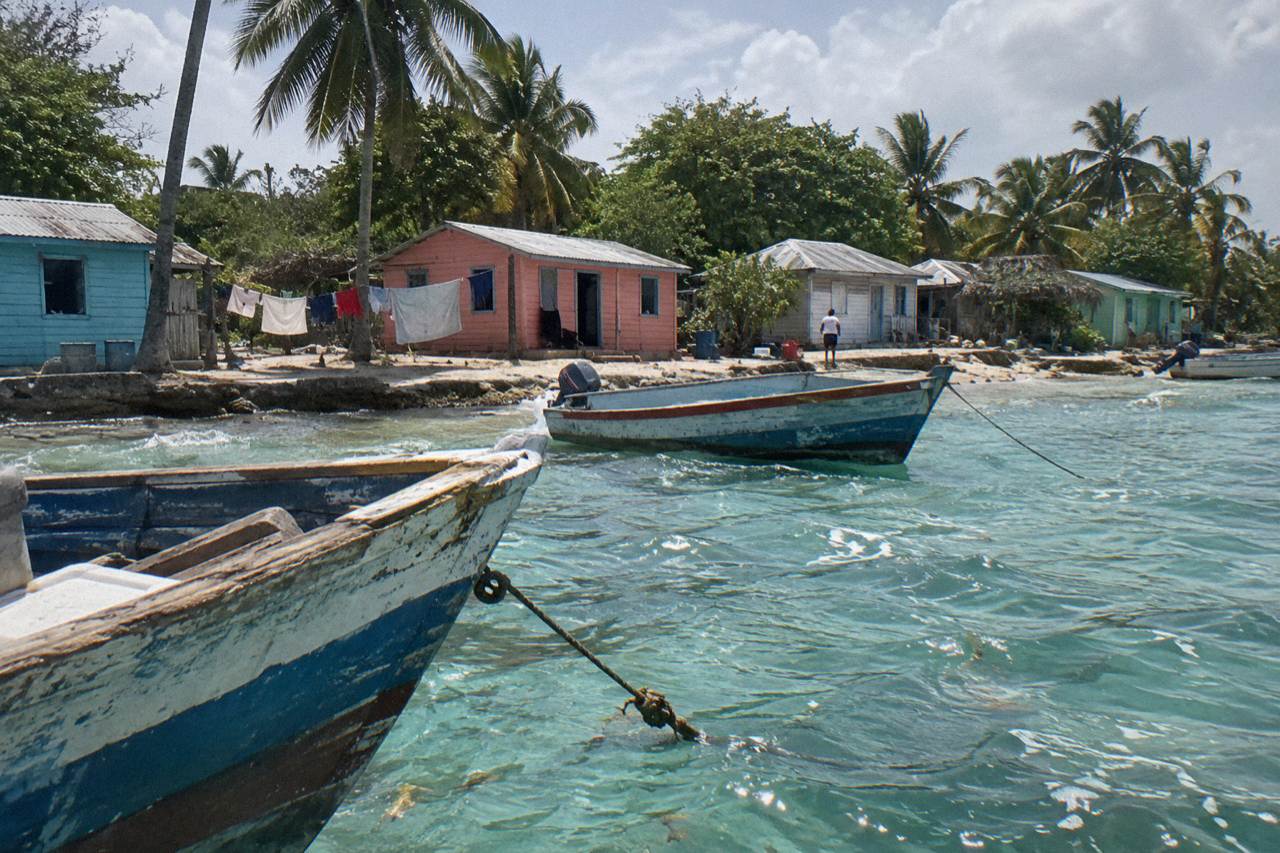 Wooden fishing boats moored in shallow turquoise water beside a small Caribbean beach village