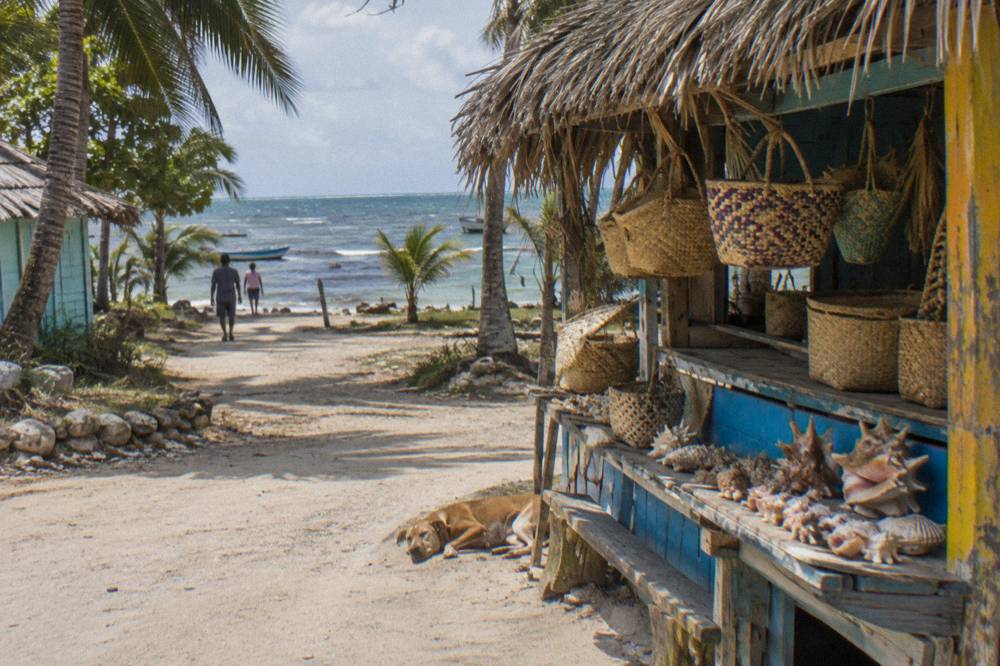 A colorful wooden stall selling shells and woven souvenirs on a sandy village street